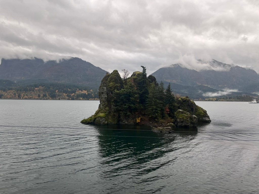 Tree-covered rocky island in the Columbia River with misty mountains in the background.